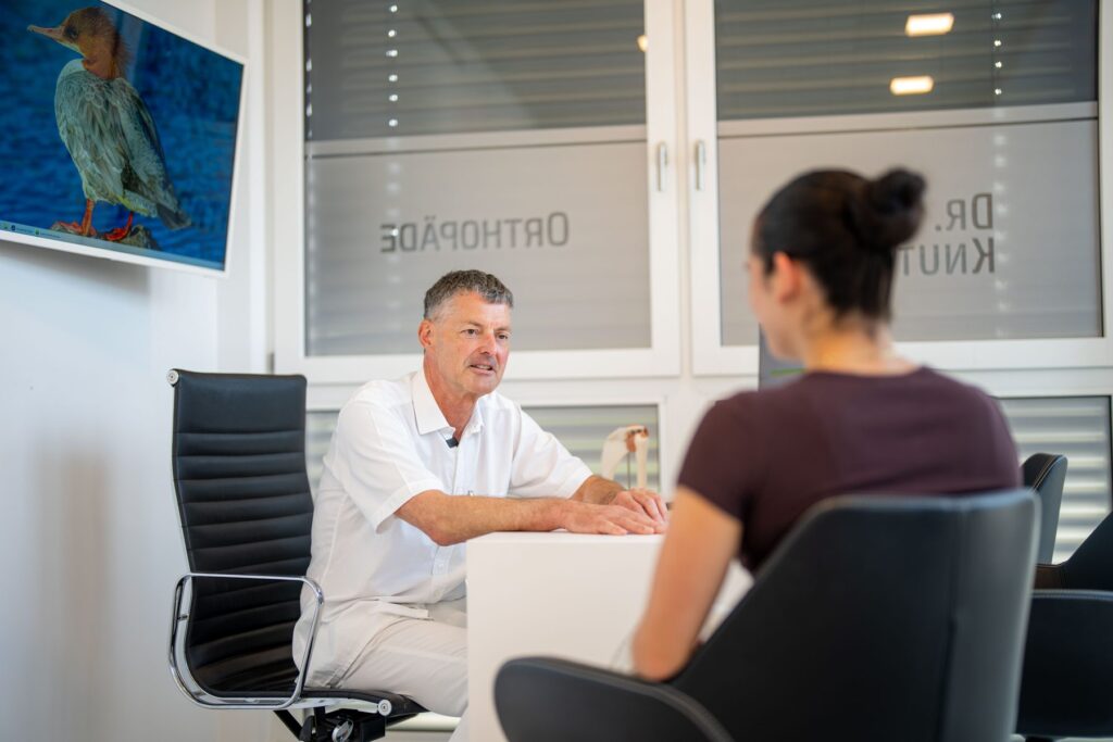 Dr. Knut Bär im Gespräch mit einer Patientin am Schreibtisch seines Sprechzimmers