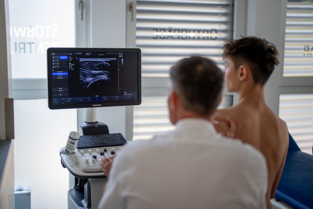 Dr. Knut Bär führt bei einem jungen Patienten eine Ultraschalluntersuchung der Schulter durch